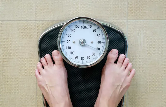 A close-up view of a person standing barefoot on an analog bathroom scale, displaying weight in kilograms, symbolizing weight tracking and personal health monitoring.